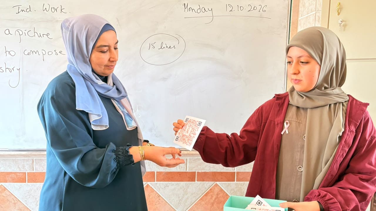 طالبة تقدّم بطاقة توعية برمز QR لمعلّمة في الصف.